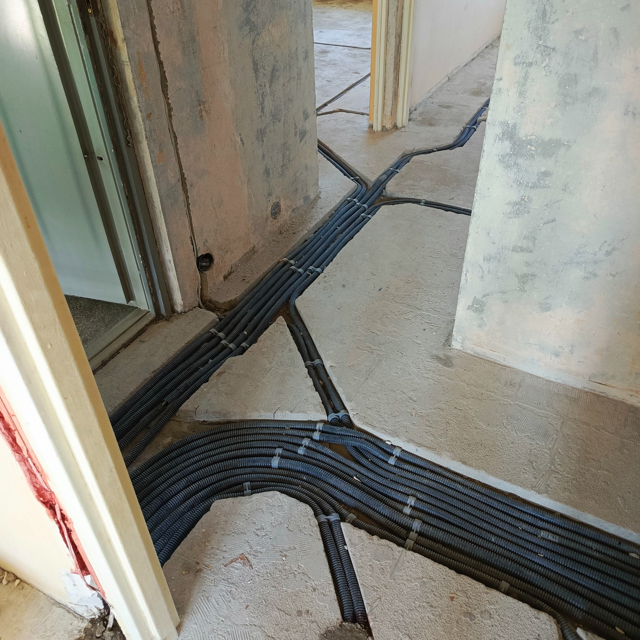 Rozprowadzenie kabli elektrycznych w peszlach, zatopionych w wylewce podłogowej podczas remontu. Widoczne korytarze i surowy stan ścian.