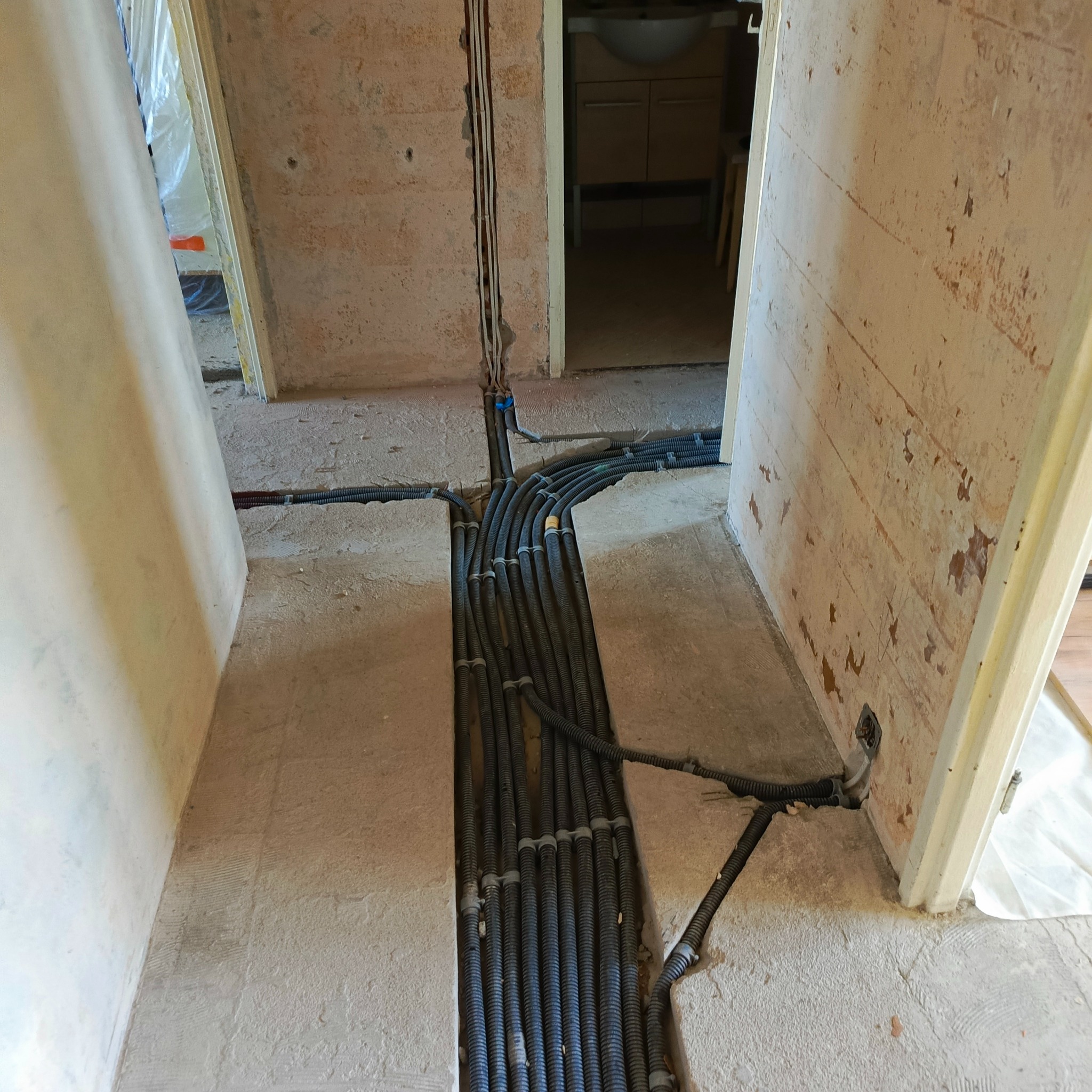 Instalacja elektryczna w bruzdach podłogowych przed wylewką. Kable w peszlach ułożone równolegle. Widoczne puszki elektryczne w ścianach.