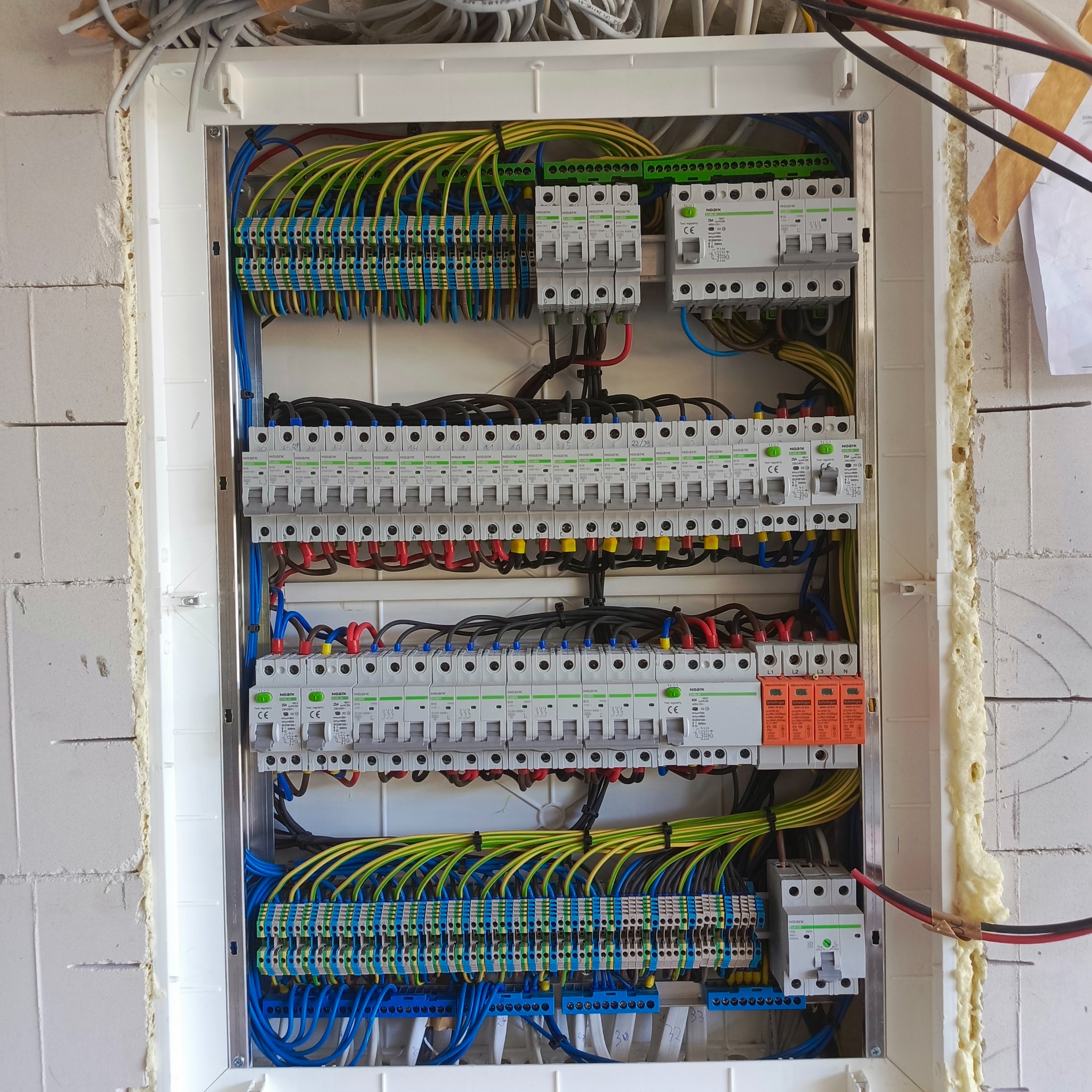 Rozdzielnica elektryczna z zainstalowanymi bezpiecznikami i okablowaniem w nowym budynku z białych bloczków. Widoczne listwy zaciskowe i przewody w różnych kolorach.