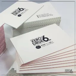 Stosy białych wizytówek z czarnym nadrukiem logo i danymi kontaktowymi firmy drukarskiej, widoczne krawędzie papieru.