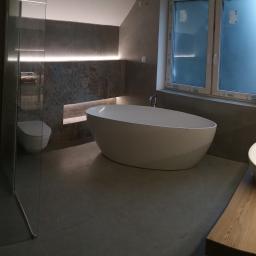 Olesek Instalacje. Projektowanie i wykonywanie instalacji sanitarnych - Nowoczesna łazienka z wolnostojącą wanną, kabiną prysznicową typu walk-in, umywalkami nablatowymi na drewnianym blacie i szarą glazurą z podświetleniem LED.