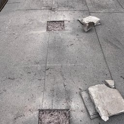 FIRMA HANDLOWO USŁUGOWA Adam Błaszczok - Płaski dach z wyciętymi fragmentami, ukazującymi warstwę izolacyjną. Widoczne narzędzia i materiały budowlane, sugerujące etap przygotowania do ocieplenia.