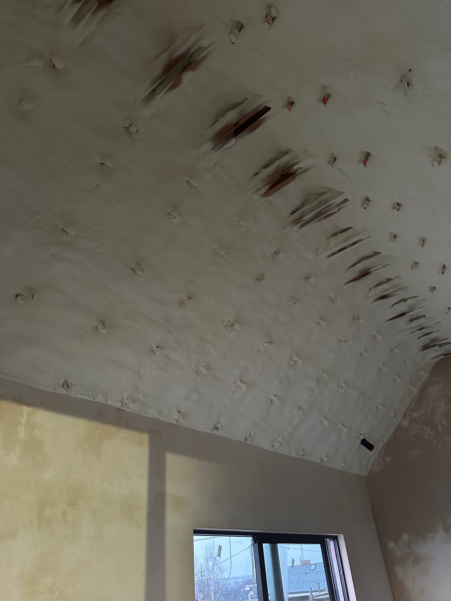 Poddasze po ociepleniu pianką PUR, widoczne drewniane elementy konstrukcyjne wystające spod warstwy izolacji. Okno w dolnej części kadru.