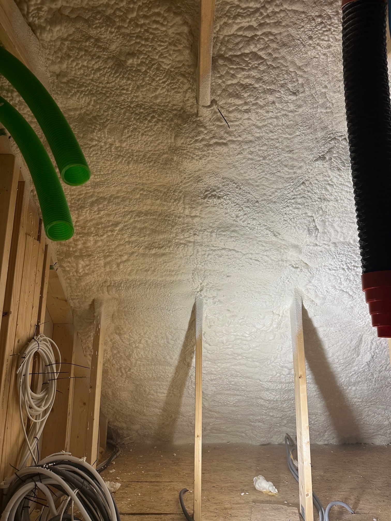 Poddasze ocieplone pianką PUR z widocznymi elementami konstrukcji drewnianej, przewodami wentylacyjnymi i kablami elektrycznymi. Widok z dołu na ocieploną powierzchnię.