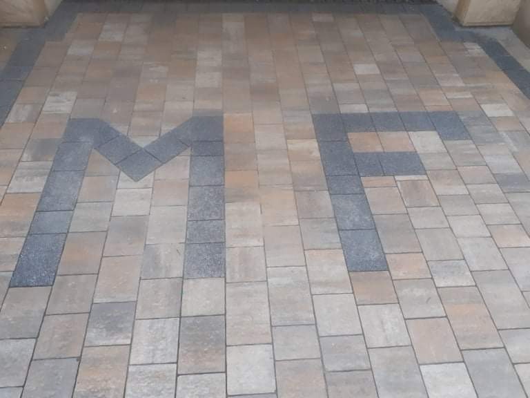 Ułożona kostka brukowa w odcieniach beżu i szarości tworząca wzór w kształcie liter 'MF'.