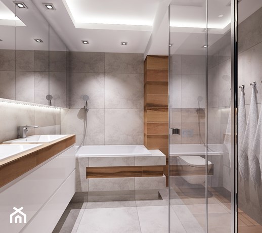 Nowoczesna łazienka z szarymi płytkami, drewnianymi akcentami, kabiną prysznicową ze szklanymi drzwiami, białymi ręcznikami i podświetleniem LED pod lustrem.