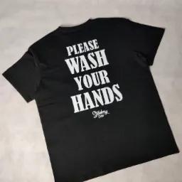 Czarna koszulka z białym nadrukiem 'PLEASE WASH YOUR HANDS' i logo 'Strawberry Crew' leżąca na szarym tle.