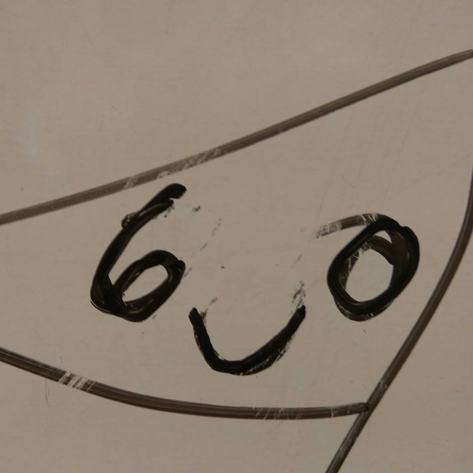 Czarny marker na białej tablicy narysował uproszczony uśmiech z cyfry 6 i litery O, otoczony niedokładną ramką.