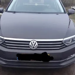 Szary Volkswagen Passat sfotografowany z przodu w Łabiszynie, z widocznym logo marki i reflektorami LED. W tle trawa, drzewa i przyczepka.