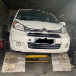 Usługi Blacharsko-Lakiernicze oraz motoryzacyjne - Biały samochód dostawczy Citroen na podnośniku najazdowym w warsztacie; widoczne ślady użytkowania pojazdu.