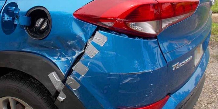 Uszkodzony, niebieski samochód Hyundai Tucson z prowizorycznie naprawionym błotnikiem i zderzakiem za pomocą srebrnej taśmy klejącej.