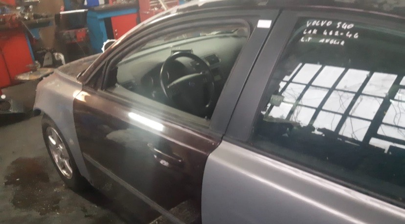 Volvo S40 z widocznymi śladami napraw blacharskich i lakierniczych, z fragmentami karoserii w szarym podkładzie, notatki na szybie.