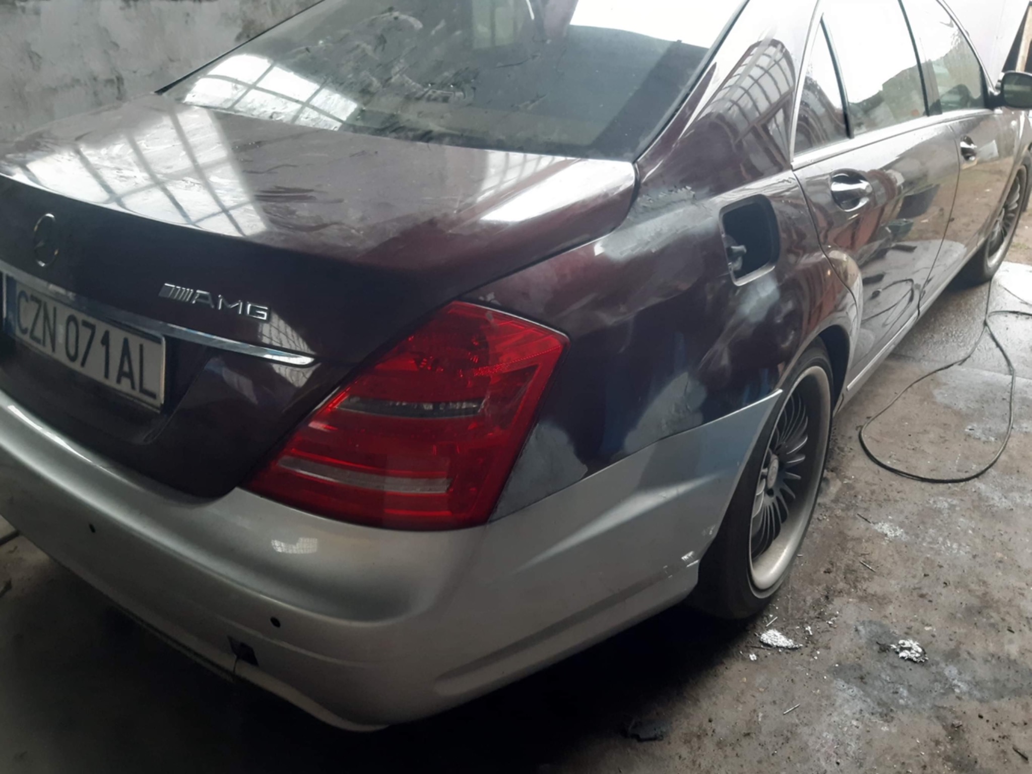 Częściowo odnowiony, bordowy Mercedes-Benz AMG w trakcie napraw blacharsko-lakierniczych; widoczny fragment tylnej części pojazdu z elementami w szarym podkładzie, zaparkowany w warsztacie.