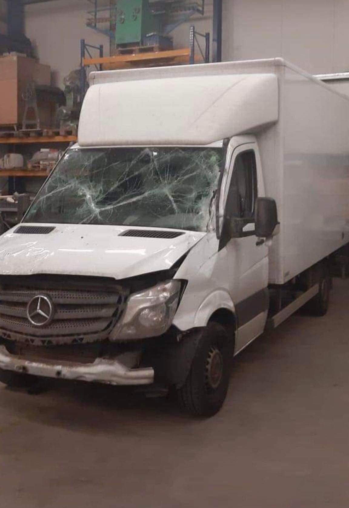 Uszkodzony biały dostawczy Mercedes Sprinter z rozbitą przednią szybą i wgniecionym przednim zderzakiem, stojący w warsztacie.