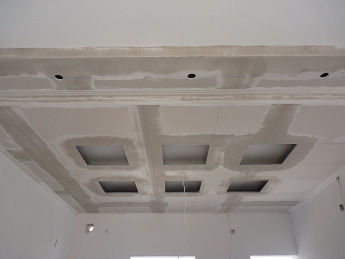 Sufit podwieszany w trakcie montażu, z widocznymi otworami na oświetlenie i łączeniami szpachlowanymi, surowy stan wykończenia.