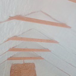Solid-House - Poddasze z drewnianą konstrukcją pokryte białą pianką izolacyjną, widoczne fragmenty ścian z płyt OSB.