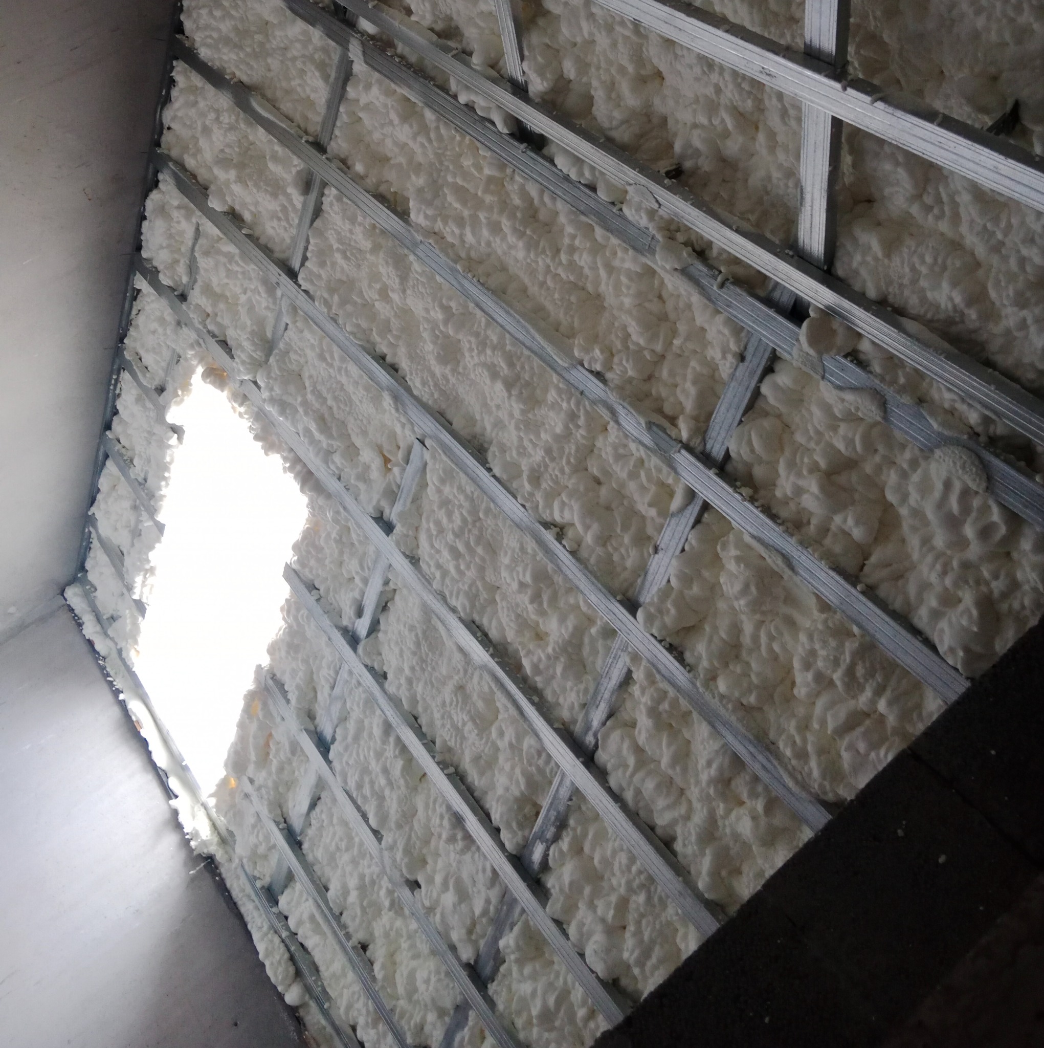 Poddasze z widoczną konstrukcją metalową wypełnioną białą pianką PUR, z jasnym prześwitem w tle.