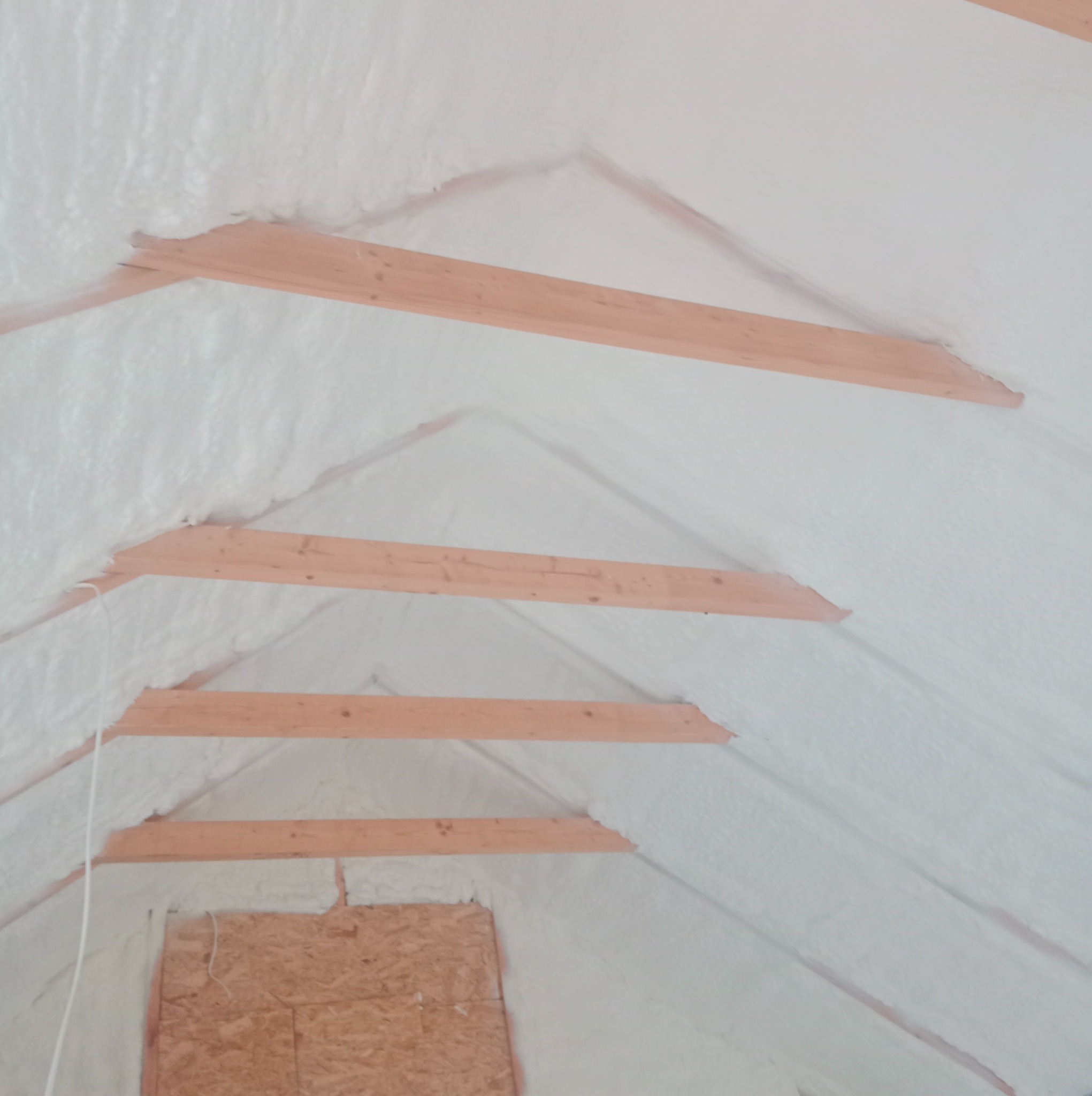 Poddasze z drewnianą konstrukcją pokryte białą pianką izolacyjną, widoczne fragmenty ścian z płyt OSB.