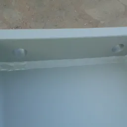 Szara, metalowa wanna z dwoma otworami na górnej krawędzi, spawana na łączeniach, na betonowym podłożu.