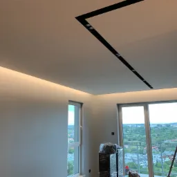 Nowoczesne oświetlenie sufitowe z czarnymi szynami i punktowymi reflektorami w jasnym wnętrzu z widokiem na miasto z balkonu.