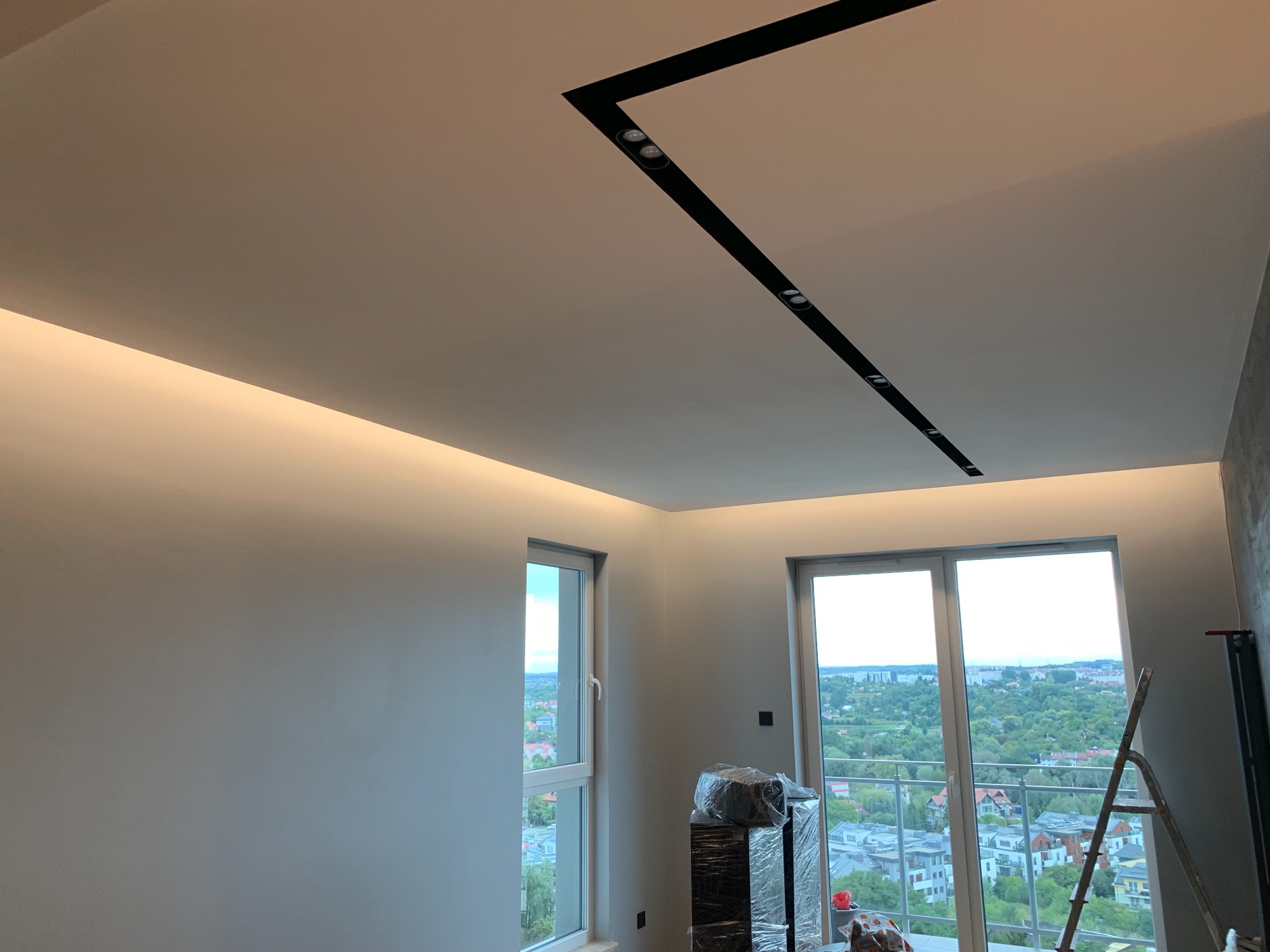 Nowoczesne oświetlenie sufitowe z czarnymi szynami i punktowymi reflektorami w jasnym wnętrzu z widokiem na miasto z balkonu.