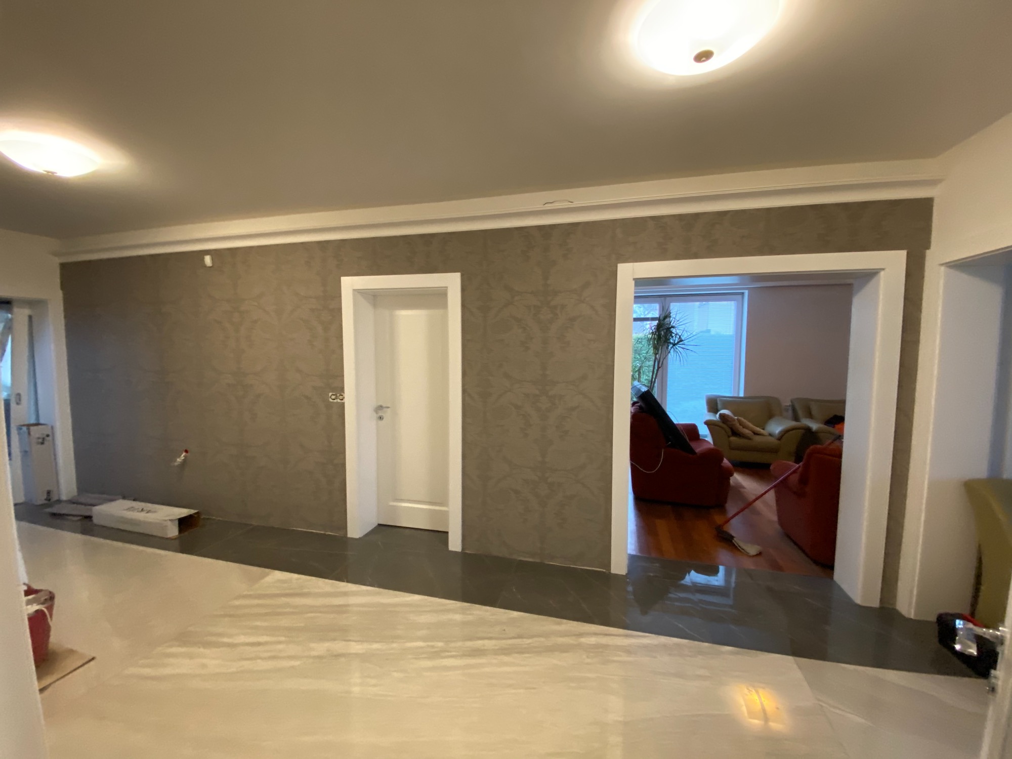 Wnętrze mieszkania po remoncie z nową marmurową podłogą, tapetą w odcieniach szarości i białymi futrynami drzwiowymi, widoczne kartony po materiałach budowlanych.