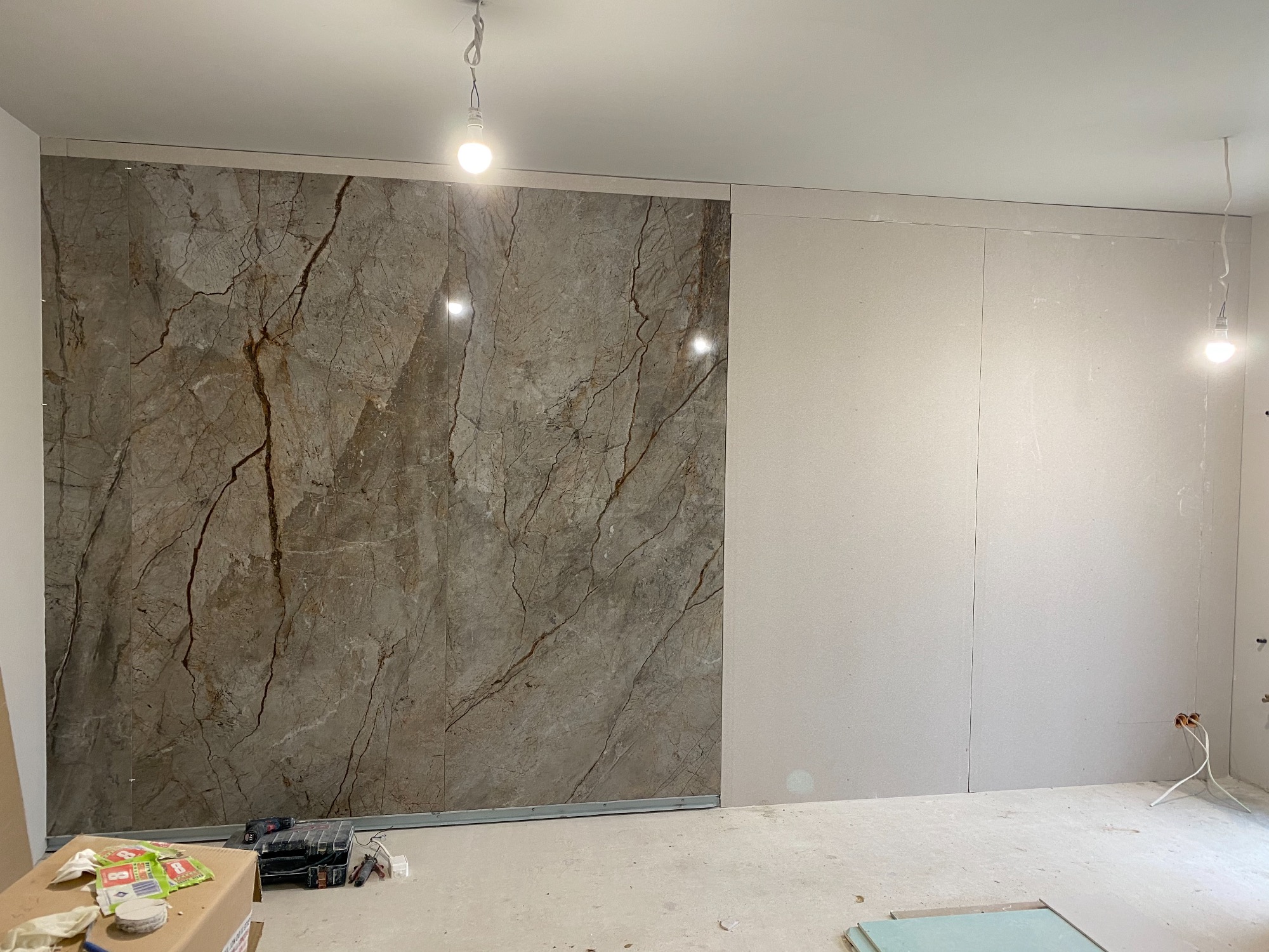 Montaż paneli ściennych imitujących marmur w trakcie remontu, widoczne narzędzia i materiały budowlane na podłodze, surowy stan ścian po jednej stronie.