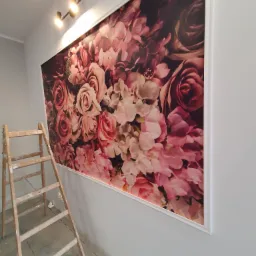 Montaż fototapety z motywem r&oacute;ż na ścianie, widoczna drewniana drabina malarska i oświetlenie sufitowe.