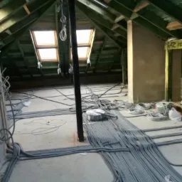 Poddasze w trakcie prac instalacyjnych: liczne przewody elektryczne ułożone na podłodze, widoczne okna dachowe i konstrukcja więźby dachowej.