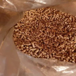 Wnętrze przezroczystego worka wypełnionego jasnobrązowym pelletem drzewnym, widoczne nierównomierne oświetlenie i faktura granulatu.