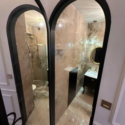 Ewelina Smażyk - Elegancka łazienka w beżach, widziana przez lustrzane drzwi z czarną ramą. Kabina prysznicowa i umywalka z lustrem w złotych akcentach.