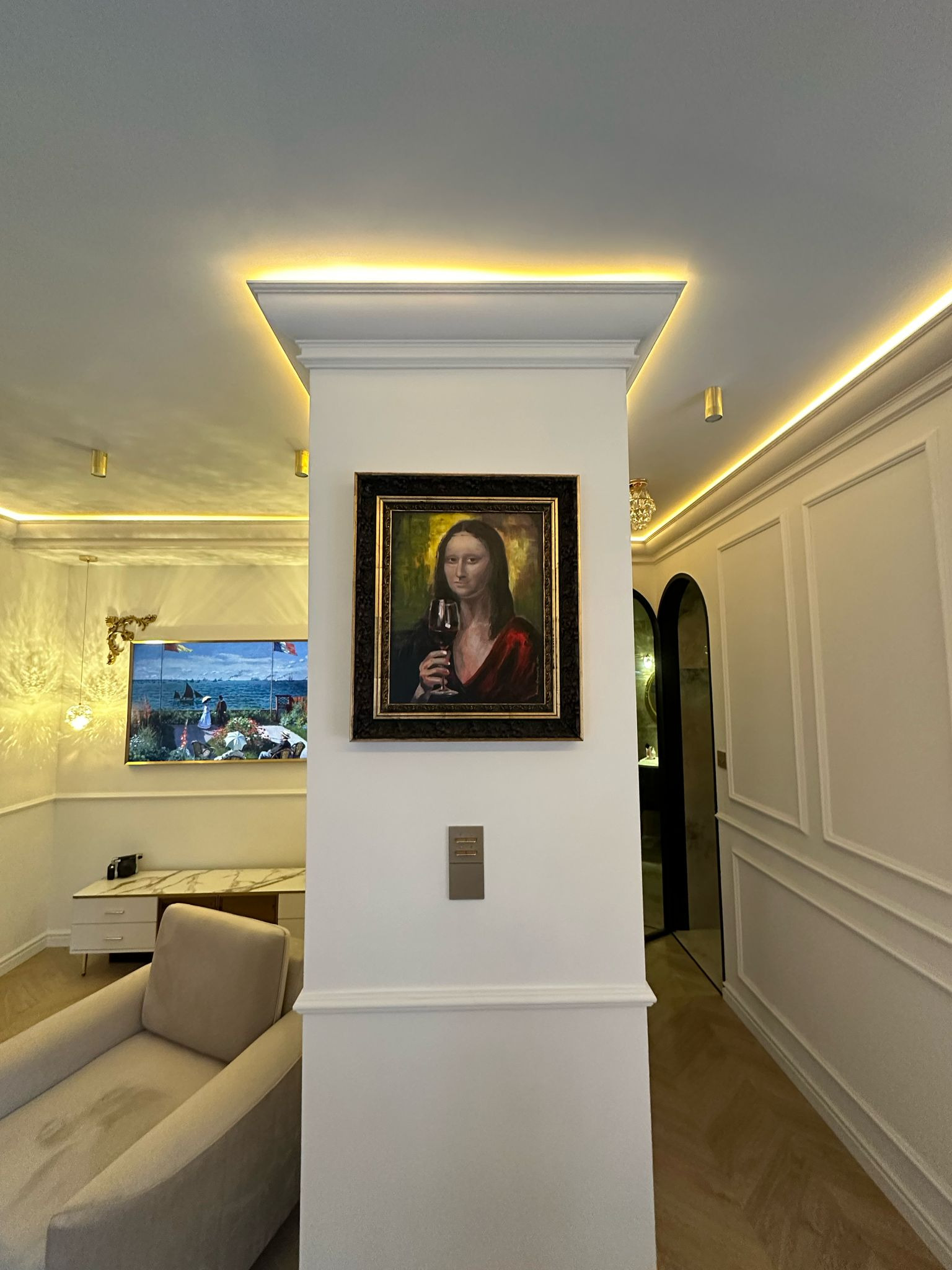 Nowoczesne wnętrze z obrazem Mona Lisy z kieliszkiem wina, oświetleniem LED i dekoracyjnymi panelami ściennymi. Widoczny fragment fotela i obraz na ścianie.