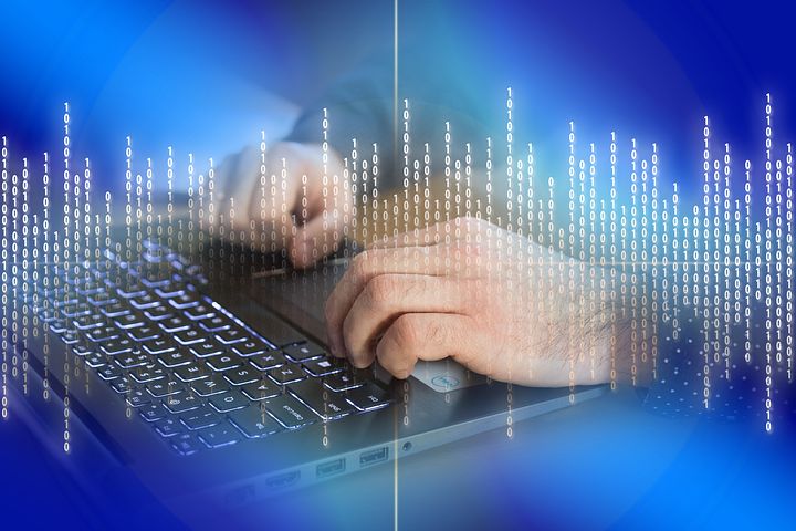 Osoba pisze na laptopie, nałożony efekt wizualizacji kodu binarnego w tle i na klawiaturze, tworząc wrażenie pracy z danymi lub programowaniem.
