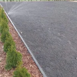 Przygotowany teren pod trawnik z zainstalowanym systemem nawadniania, obrzeża z kostki i posadzone małe drzewka iglaste.