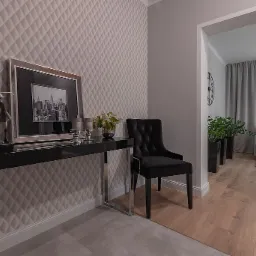 Elegancki przedpokój z pikowaną tapetą, czarnym stolikiem konsolowym z dekoracjami, czarnym krzesłem i widokiem na salon w odcieniach szarości.