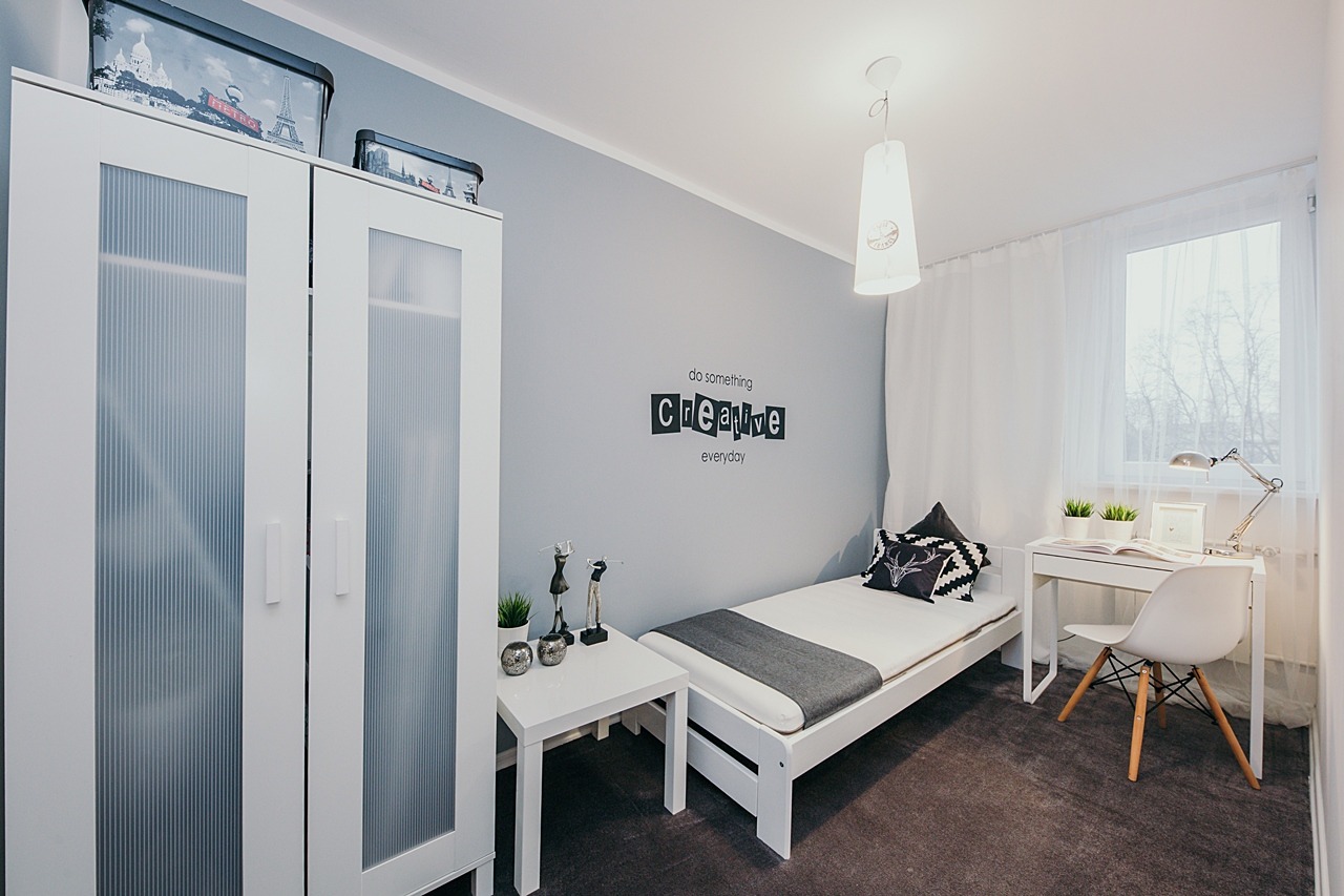 Nowoczesny pokój młodzieżowy w odcieniach szarości i bieli, z łóżkiem jednoosobowym, biurkiem, szafą z ryflowanymi szybami i dekoracyjnym napisem na ścianie.