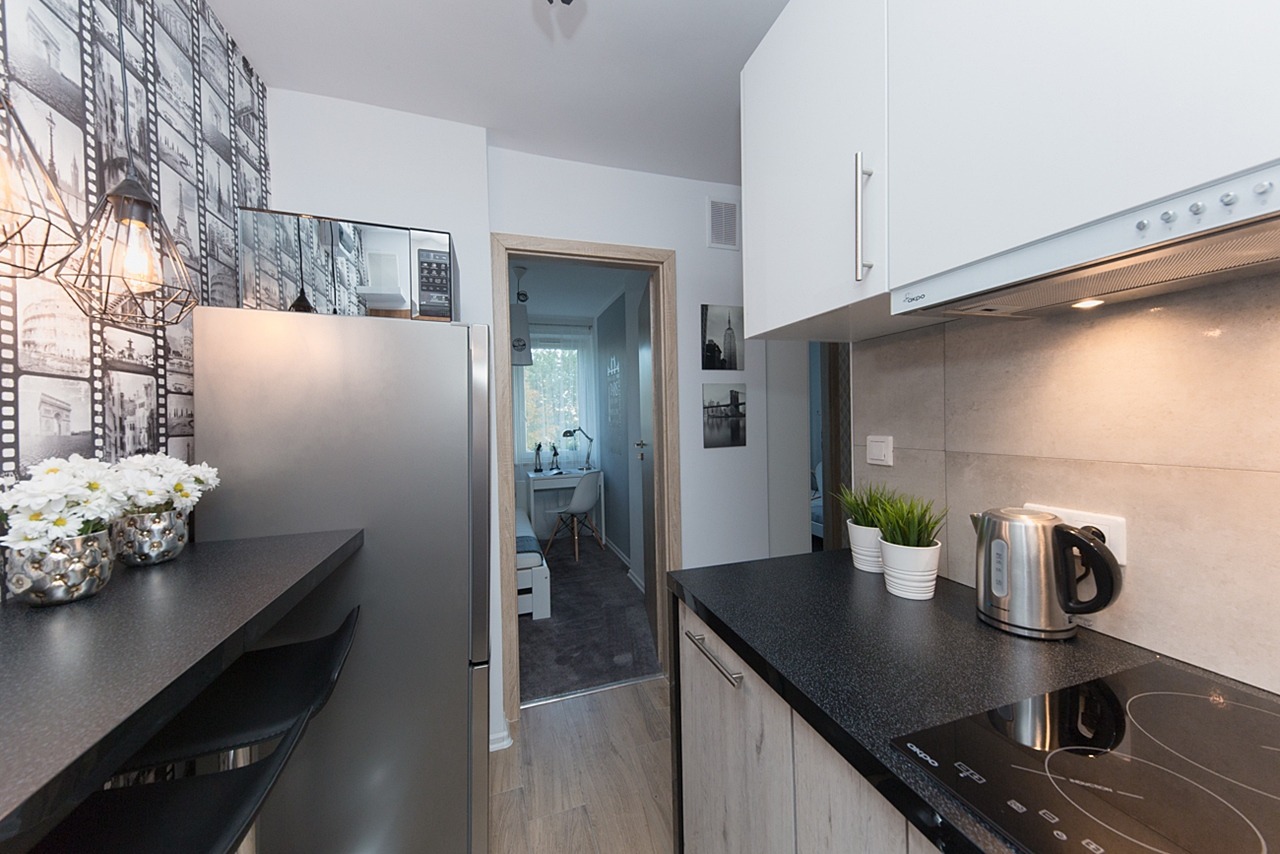 Nowoczesna kuchnia z czarnym blatem, srebrną lodówką i tapetą w motywy filmowe, widok na pokój z biurkiem.