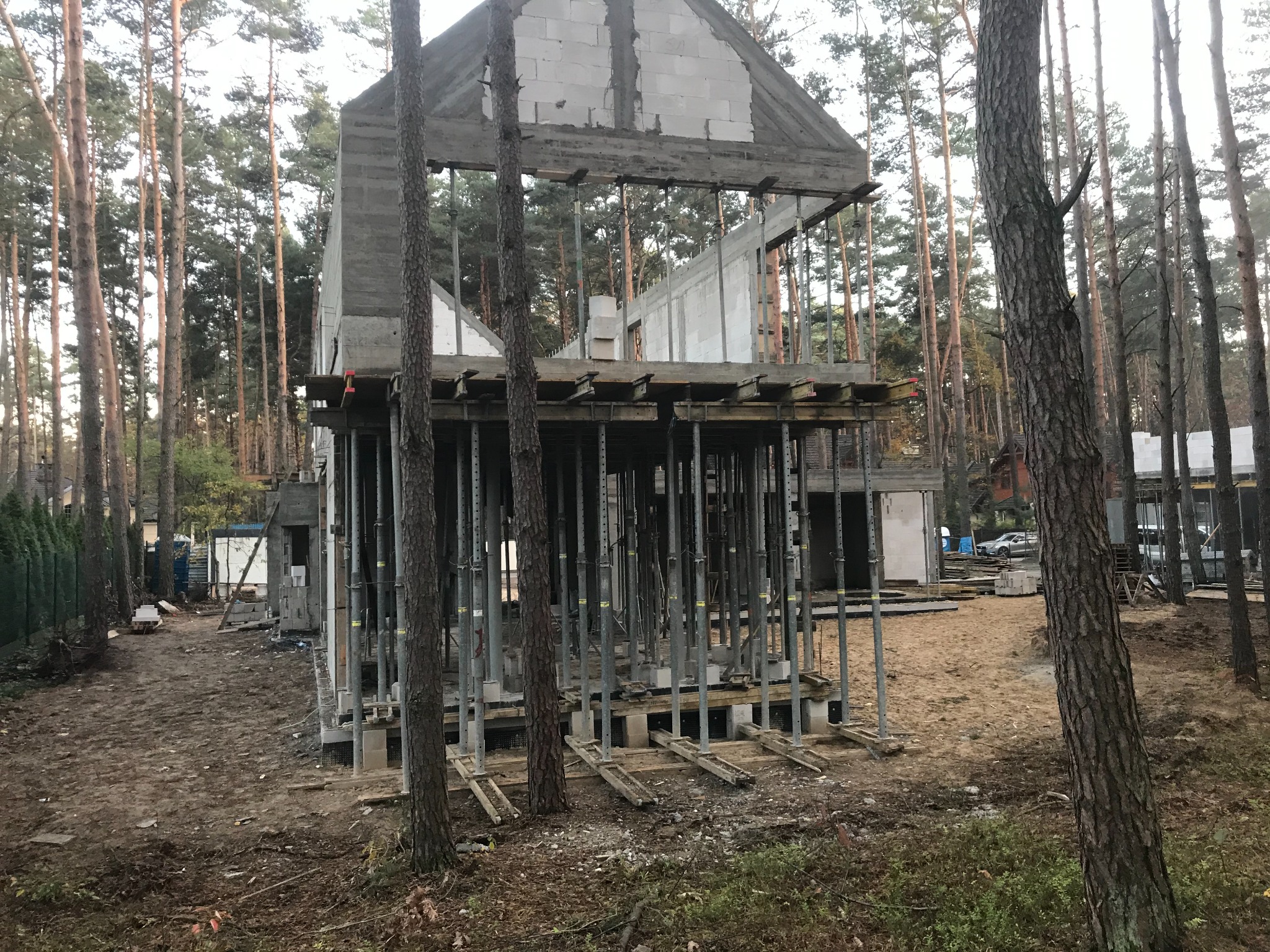 Surowy stan dwukondygnacyjnego domu z betonu komórkowego w lesie, widoczne stalowe podpory szalunkowe i drewniane elementy konstrukcyjne.