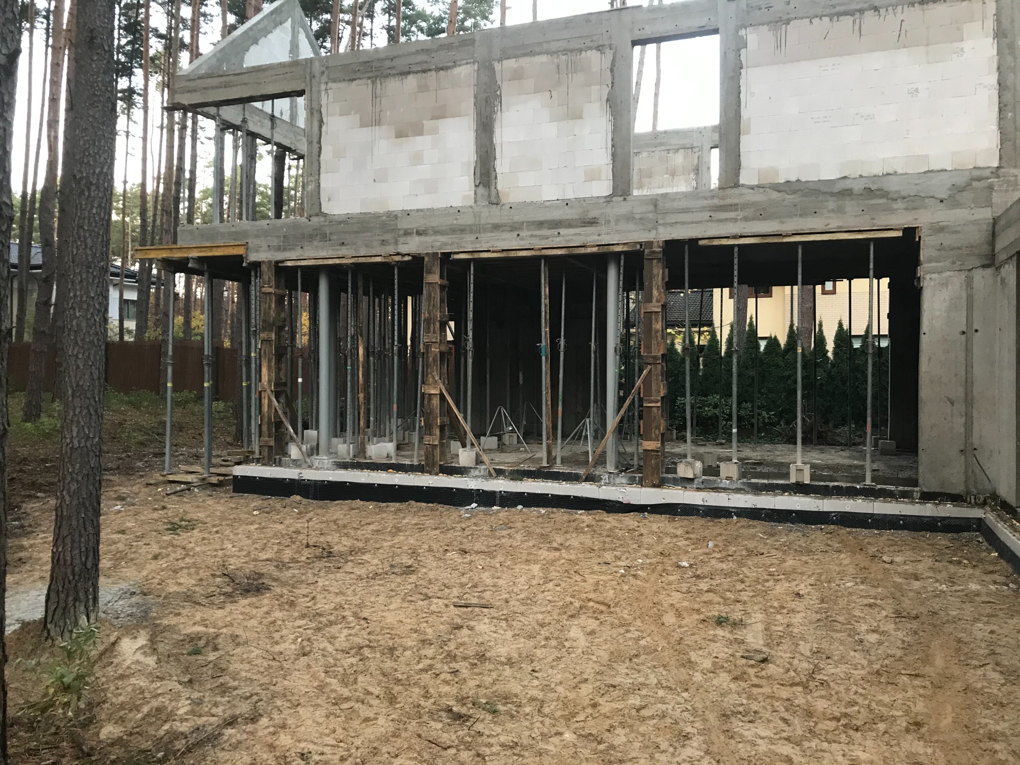Surowy stan domu w trakcie budowy z betonu komórkowego, widoczne szalunki i podpory, teren budowy piaszczysty.