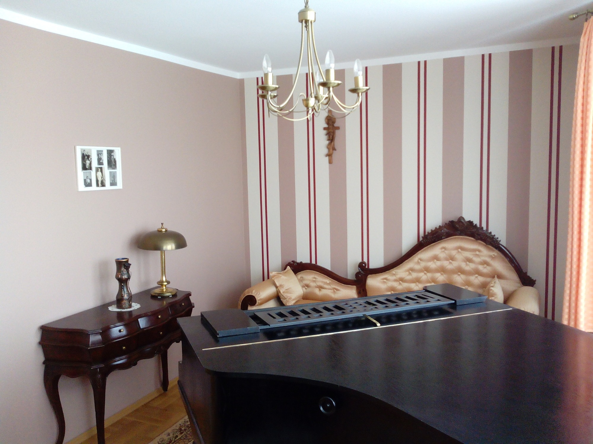 Klasyczny salon z pianinem, tapetą w pionowe pasy i antycznym kredensem z lampką.