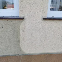 Fragment elewacji z oknami, widoczna różnica w odcieniu tynku po czyszczeniu lub malowaniu.