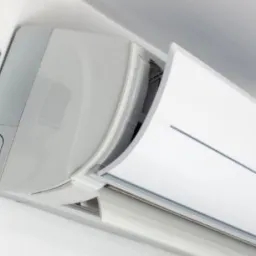 Biały klimatyzator ścienny z otwartą klapą, widoczny pilot z wyświetlaczem LCD zamontowany na ścianie obok urządzenia.