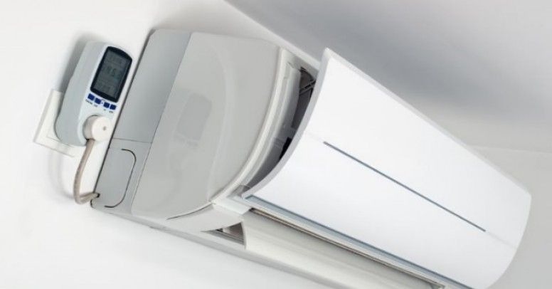 Biały klimatyzator ścienny z otwartą klapą, widoczny pilot z wyświetlaczem LCD zamontowany na ścianie obok urządzenia.