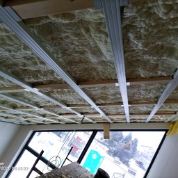 JEST POZIOM Mariusz Zajączkowski - Poddasze z widoczną konstrukcją metalową i pianą izolacyjną, widok z dołu na okno. Etap ocieplania poddasza z użyciem piany PUR.