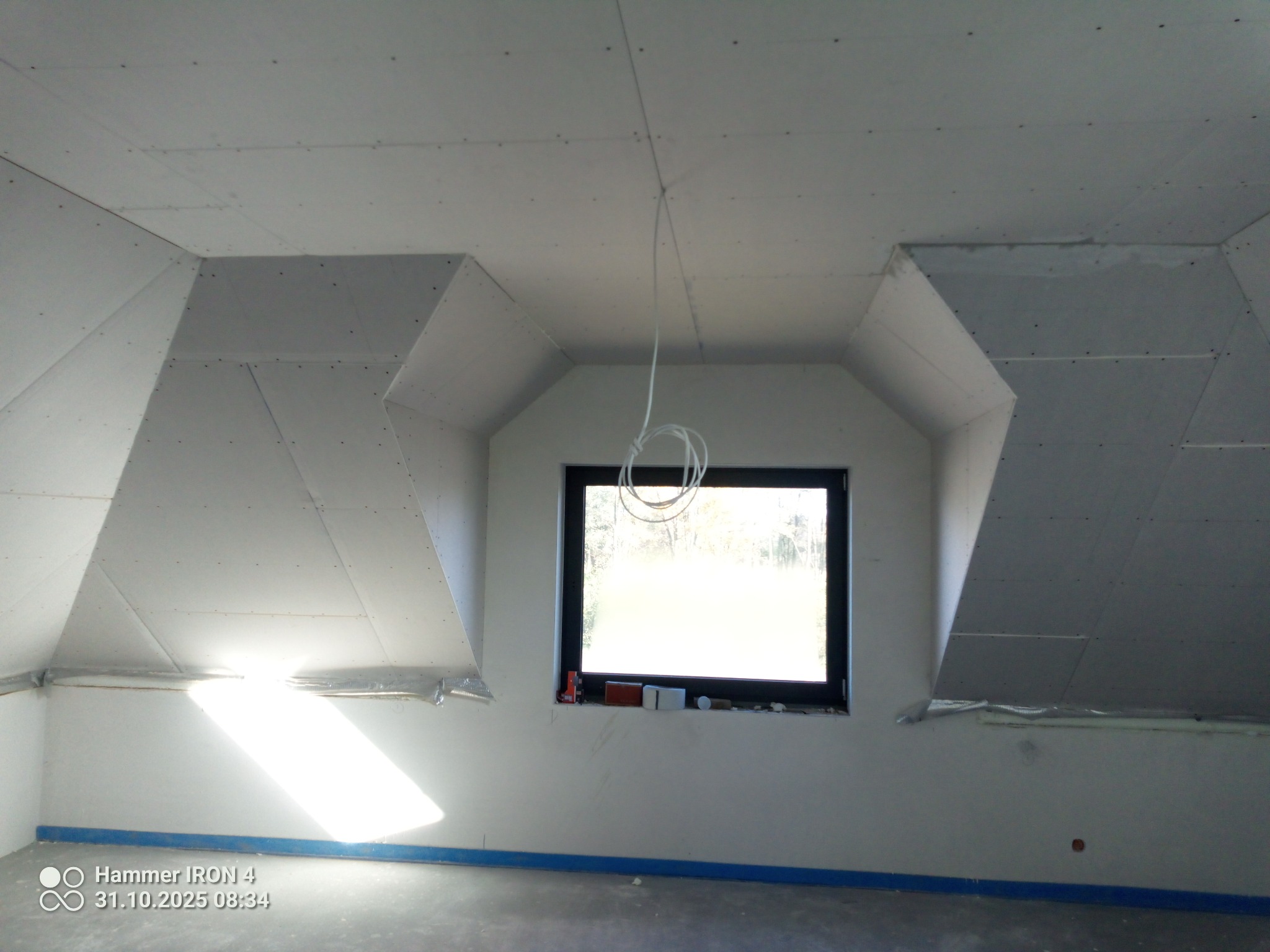 Poddasze po montażu płyt karton-gips z widocznym oknem i wystającymi przewodami. Ściany przygotowane do dalszych prac wykończeniowych.