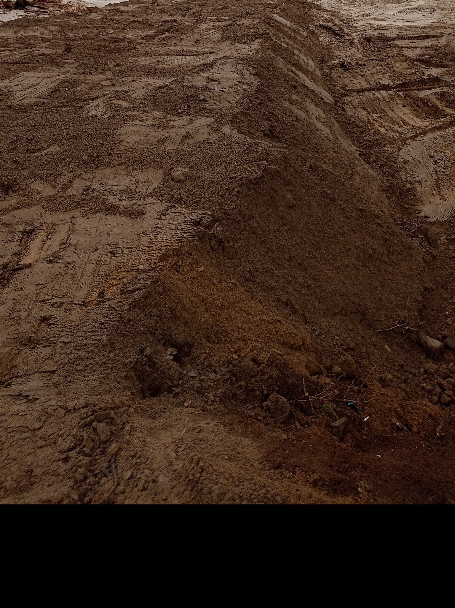 Kupa ziemi z widocznymi śladami opon pojazdu budowlanego, na nierównym terenie.