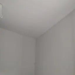 Pomieszczenie po szpachlowaniu, widoczny narożnik i fragment sufitu z wystającym przewodem elektrycznym.