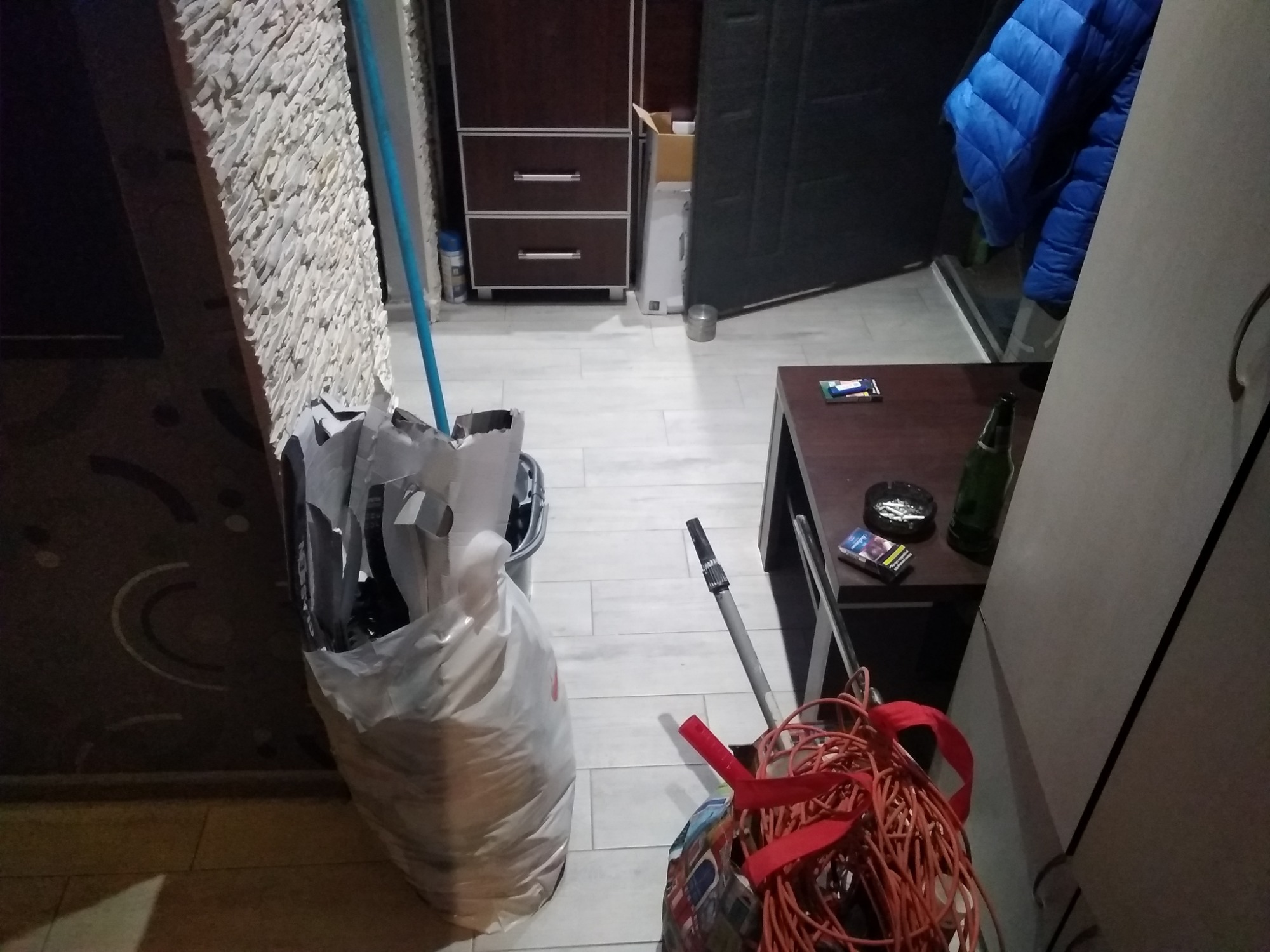 Wnętrze pokoju w trakcie lub po remoncie, widoczny worek z odpadami budowlanymi, kabel elektryczny, narzędzie malarskie i fragment ściany z dekoracyjnym wykończeniem.