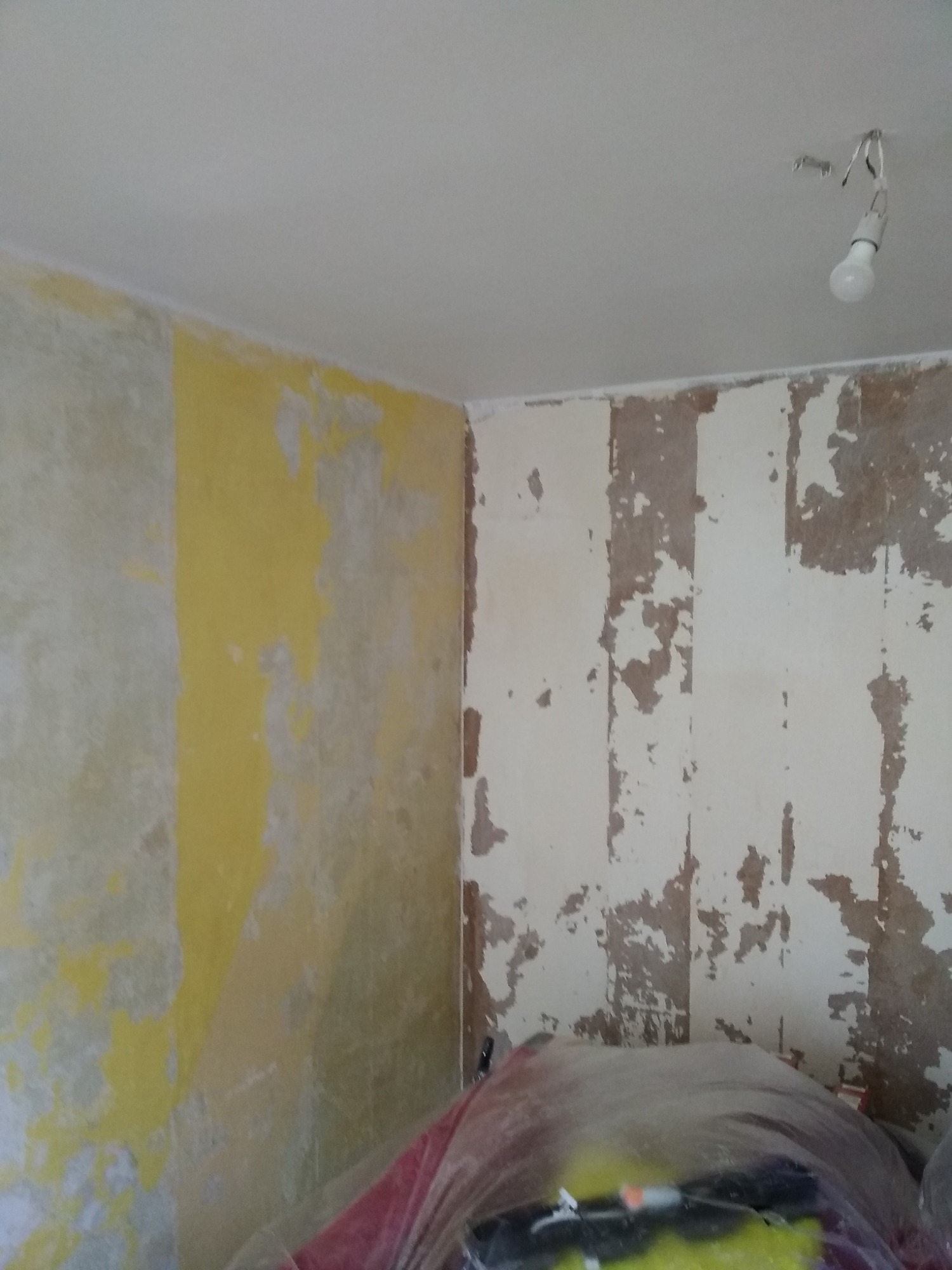 Przygotowanie ścian do malowania w Żaganiu: usunięte fragmenty starej farby, odsłonięte warstwy, widoczna żarówka na suficie.