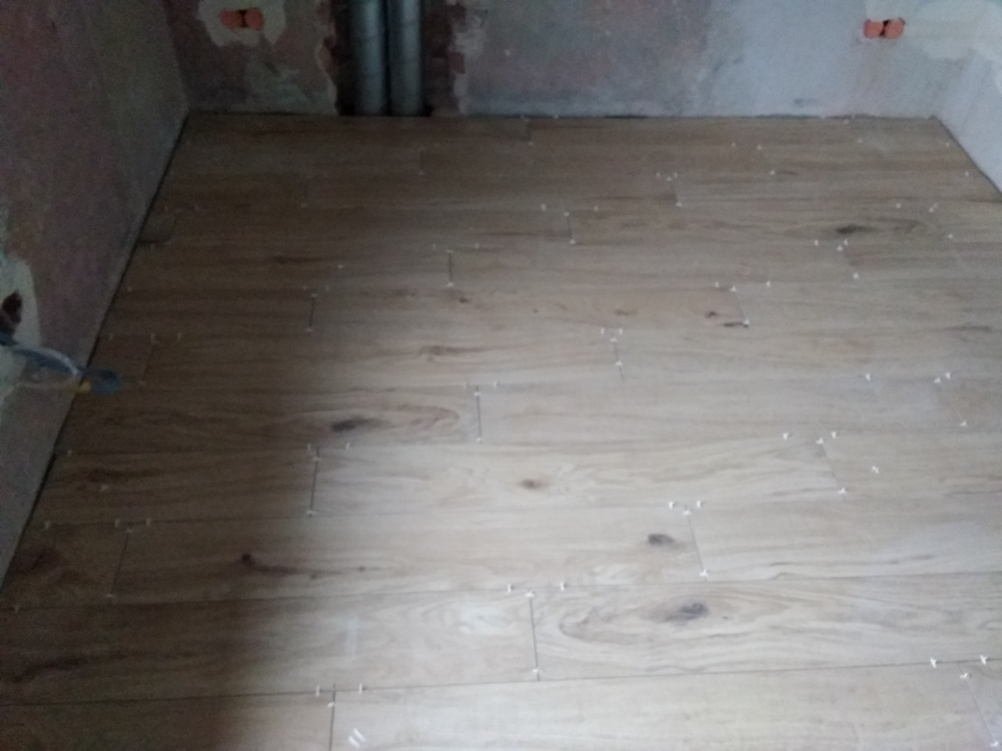 Układanie płytek imitujących drewno na podłodze w trakcie remontu, widoczne krzyżyki dystansowe i surowe ściany.